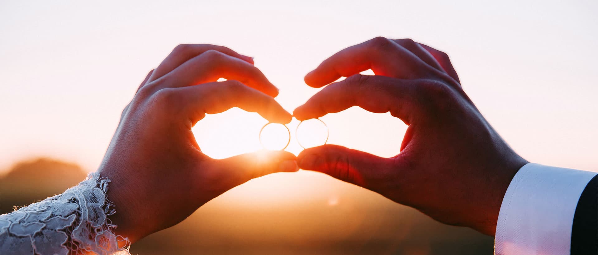 Couple holding wedding rings at golden hour